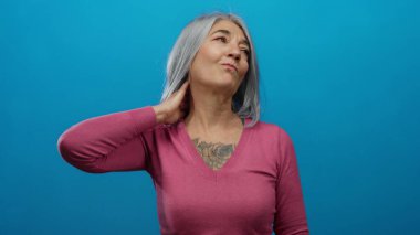 Parlak mavi arka planda, eli boynundaydı. Gri saçları ve pembe süveteri vardı. Düşünceli bir yüz ifadesi vardı..