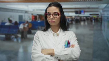 Beyaz üniformalı, kırmızı gözlüklü İspanyol kadın bilim adamı. Havalimanında kapalı alanda el kol hareketi yapmıyor. Parmaklarıyla onaylamıyor..