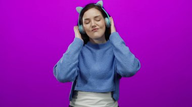 Renkli kulaklıklarla müzikten hoşlanan bir kadın canlı pembe arka plana karşı keyfi ve rahatlığı gündelik bir şekilde ifade ediyor..