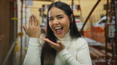 İnşaat alanında, aşk heyecanını ve gelecekteki bağlılığı sembolize eden mutlu bir şekilde nişan yüzüğü gösteren bir kadın.