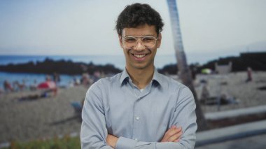 Güneşli yaz sahillerinde kolları çapraz duran gözlüklü bir adam arkasında insanlar, özgüven..