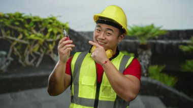 Sarı miğfer ve yelek giymiş gülümseyen adam şehir dışında bir tüp tutuyor. İnşaatı eğlence aktiviteleriyle harmanlıyor..