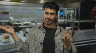 Kalıp desenli ceketli adam, mutfak tezgahı ve aletlerle avuç içi açık bir şekilde elini uzatıyor..