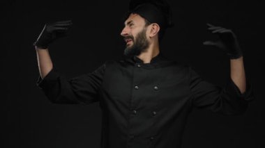Sakallı İspanyol erkek aşçı siyah eldiven giyip siyah bir arka plana karşı üniforma giyiyor. Mutfak uzmanlığı ve tutkusunu aktarıyor..