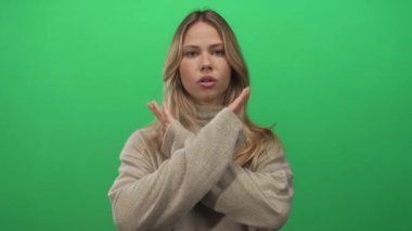 Balıkçı yaka kazak giyen kadın yeşil bir fotoğraf stüdyosunda kollarını kavuşturuyor; reddediliyor.