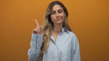 Sarışın kadın çizgili gömlekli parmak turuncu duvarlı parlak ışıklı stüdyo ortamını işaret ediyor..