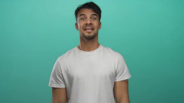 Genç İspanyol adam canlı yeşil arka plana karşı güvenle gülümsüyor. Ayrı bir ortamda günlük beyaz gömlek giyiyor. Neşe saçıyor ve pozitif enerji yayıyor.