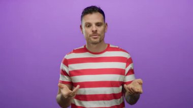 Kırmızı çizgili tişörtlü İspanyol genç adam izole edilmiş mor bir arka plana karşı duruyor düşünceli bir ifade ve anlamlı el hareketleriyle.