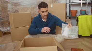 Genç adam yeni bir oturma odasında kutuları açıyor. Etrafı karton, balonlu naylon ve sarı bir bavulla çevrili. Boş bir dairede yeni bir başlangıç olduğunu gösteriyor..