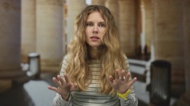 Koridorda sakin bir şekilde el kaldıran bir kadın. Sarışın genç denek, içerideki portrede gerginliğin azaldığını gösteriyor..