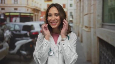 Şehir sokaklarında steteskopla gülümseyen kadın doktor, açık hava ortamında pozitifliğini ifade ediyor, kamu sağlık hizmetleriyle uğraşırken sıcaklığı ve arkadaşlığı iletiyor..