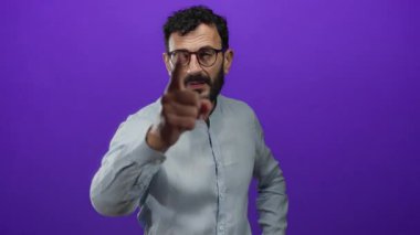 Sakallı ve gözlüklü İspanyol bir adam canlı mor arka plan, odaklanma ve kararlılık konusunda kameraya güvenle bakıyor..