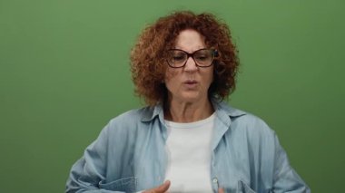 Yeşil arka planda kot ceket giymekten rahatsız olan bir kadın, tenha bir ortamda soğukluk gösteren orta yaşlı bir İspanyol kadını resmediyor..