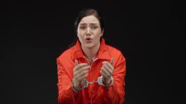 Turuncu elbiseli kadın kelepçeli, esmer saçlı siyah arkaplan, duygularını ifade eden kişi gergin ve dramatik bir ortamda odaklanmış görünüyor..