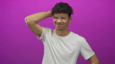 Beyaz tişörtlü ve gözlüklü İspanyol bir adam stüdyoda tereddütlü bir gülümsemeyle tepeden tırnağa kaşıyor..