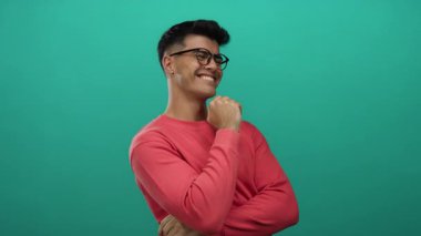 Genç bir adam pembe bir kazakla canlı yeşil bir arka plana karşı güvenle gülümsüyor. Neşeli ve rahat bir atmosfer sergiliyor. İspanyol mirasını vurguluyor..