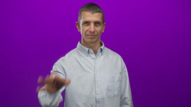 Çizgili gömlekli bir adam canlı mor arka plana karşı şakacı bir şekilde poz veriyor, kendinden emin ve neşeli bir ifade sergiliyor..