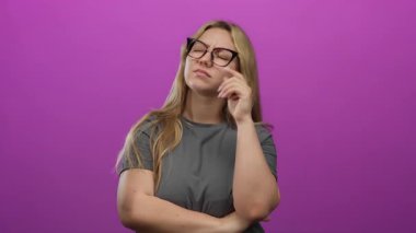 Düşünceli bir ifadeyle düşünen, sarı saçlı, gözlüklü, parlak pembe bir arkaplanda izole edilmiş, tefekkür etmeyi ve karar vermeyi öneren bir kadın..