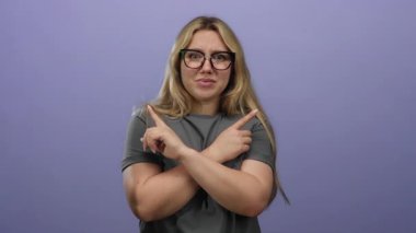 Gözlüklü, sarı saçlı bir kadın, izole edilmiş mor bir arka plan karşısında duruyor, kollarını kavuşturuyor ve farklı yönlere bakıyor, tuhaf bir ifadeyle..