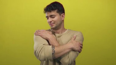 Adam omuzlarını sarıyor arka planda kendini kucaklıyor genç İspanyol sarısı erkek portresi sergiliyor.