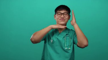 Yeşil önlüklü, steteskoplu genç Çinli adam izole edilmiş yeşil arka plan duvarına gülümsüyor..