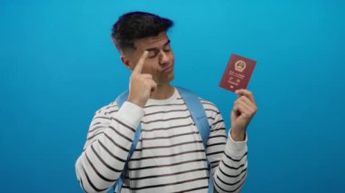 Mavi arka planı olan genç bir adam, elinde bir Çin pasaportu ile kafasına dokunuyor, çizgili bir gömlek ve mavi bir sırt çantası giyiyor, seyahat ve kimlik temasını ima ediyor..