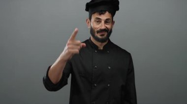 Siyah üniformalı İspanyol erkek aşçı, gri zemine karşı düşünceli bir şekilde el kol hareketi yapıyor. Mutfak sanatlarında yenilik öneriyor..