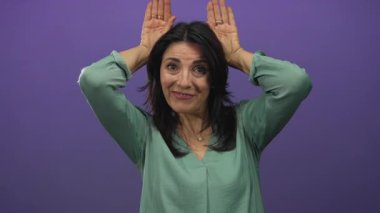 Mor bir stüdyo duvarına karşı elleri havada gülümseyen yeşil bluz giyen İspanyol kadın..