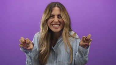 Mor bir fotoğraf stüdyosunda pençeli el hareketi ve coşkulu bir sırıtış gösteren genç sarışın kadın..