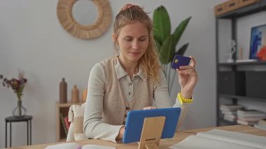 İnternet üzerinden ödeme taraması sırasında sarışın genç profesyonel kart tutarken, evde alışveriş için tablet kullanan kadın.