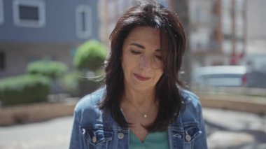 Orta yaşlı İspanyol kadın elini kaldırıyor ve bulanık binalarla dolu güneşli bir sokakta gülümsüyor; iyimserlik.