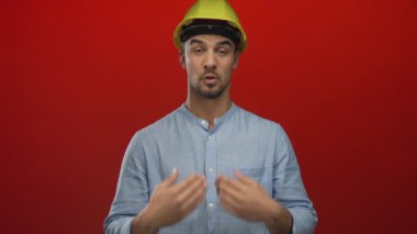 Şapkalı genç İspanyol bir adam, izole edilmiş kırmızı bir arka planda kutlama yapıyor, günlük mavi gömleğiyle neşe ve başarı somutlaştırıyor..
