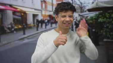Gözlüklü ve beyaz süveter giyen genç İspanyol adam şehir caddesinde bulanık kafelerle el ele hareketler dinliyordu..