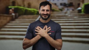 Dışarıda sakallı bir adam gülümsüyor ve bir şehir caddesinde kendini kucaklıyor, huzur ve mutluluk taşıyor..