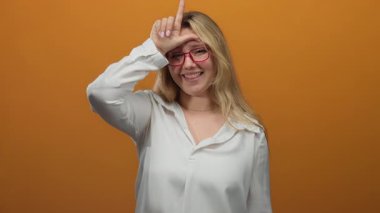 Ezik işareti yapan ve turuncu arka planda kameraya bakan bir kadın..