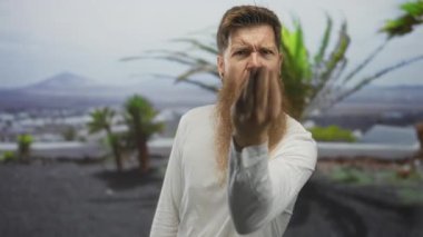 Uzun sakallı adam yumruğunu sıkar ve palmiye ağaçlarıyla yeşil parkta bağırır..