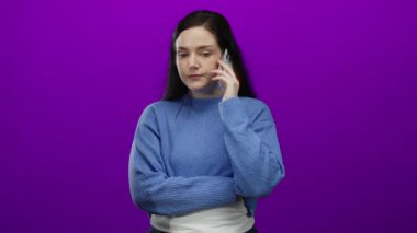 Akıllı telefondan konuşan, gözleri kapalı mavi kazak giyen, canlı mor arka planda duygusal ve derin düşüncelere dalmış bir kadın gündelik modern yaşam tarzını canlı bir şekilde yakalıyor.