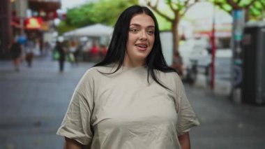 Kalabalık bir caddede arka planda yeşil ağaçlarla gülümseyen bir kadın, günlük bej bir kıyafetle şehir yaşamını ve gençlik enerjisini somutlaştırıyor..