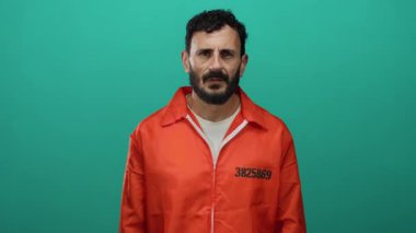 Turuncu hapishane tulumlu İspanyol bir adam yeşil arka planda ciddi ciddi kameraya bakıyor, ifadesiyle kasvetli ve düşünceli bir ruh hali içinde..