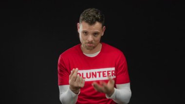 Kırmızı gömlekli genç adam siyah arka plana karşı para hareketi yapıyor. Espri anlayışı ve yüz ifadeleri ve el hareketleriyle karizma sergiliyor.