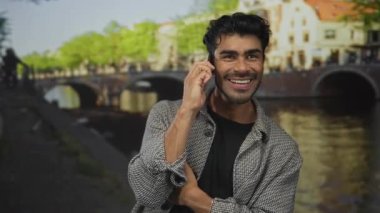 Şehir binalarının ötesinde mutluluk bağlantıları olan güneşli cadde kanallarında insan akıllı telefonu kulağına tutuyor.