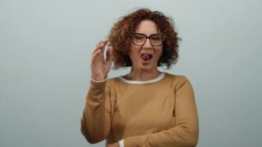 Orta yaşlı bir kadın, izole edilmiş beyaz duvara karşı komik bir yüz ifadesi sergiliyor. Kişiliği ve duyguları neşeli bir şekilde vurguluyor..