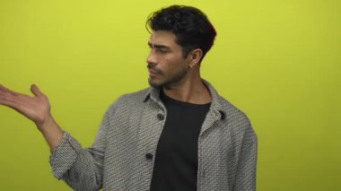 Sarı ceketli İspanyol genç adam, sarı stüdyoda avuç içini ve parmağını açık tutuyor; belirsizlik..