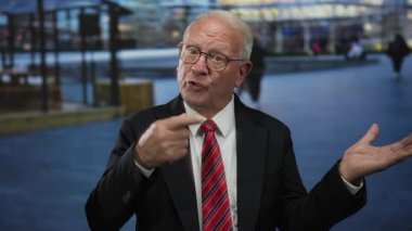 Takım elbiseli kıdemli bir adam açık havada konuşurken hareketli bir şekilde konuşur, dinamik bir tartışma ya da müzakere önerir..