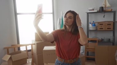 Yeni dairede selfie çeken genç bir kadın. Etrafı gündüz vakti oturma odasındaki kutularla çevrili.