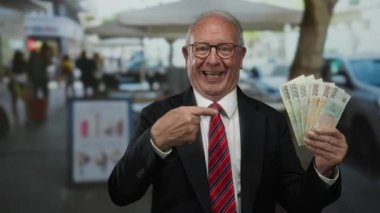 Czech Koruna banknotlarını elinde tutan kıdemli bir adam hareketli bir açık hava restoranının terasında iş ortamında neşe ifade ediyor..