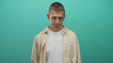 İzole edilmiş yeşil arka plana karşı duran bej gömlekli beyaz bir adam stüdyo ortamında nötr bir ifade sergiliyor..