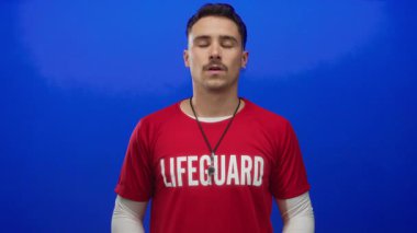 Kırmızı tişörtlü genç İspanyol cankurtaran sakin ve odaklanmış bir şekilde mavi arka plan duvarına karşı meditasyon yapıyor.