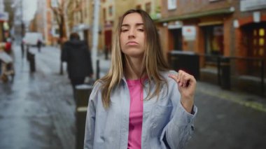 Bir kadın şehir caddesinde dikkatli bir jest yapıyor, tetikte ve dikkat çekiyor, bulanık bir geçmişi var, şehir yaşamını ve dinamik çevreyi gösteriyor..