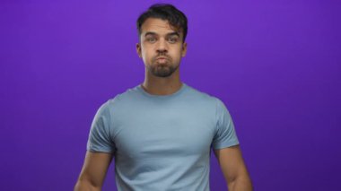 Genç adam yanaklarını şişiriyor ve parmaklarını izole edilmiş mor arkaplan önünde dokunduruyor..